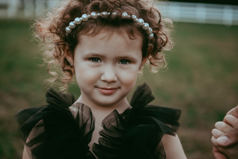 a girl in black dress and white pearl headband is looking straight during a fall outside family session by Bella Luna Photography in Fairfax, VA