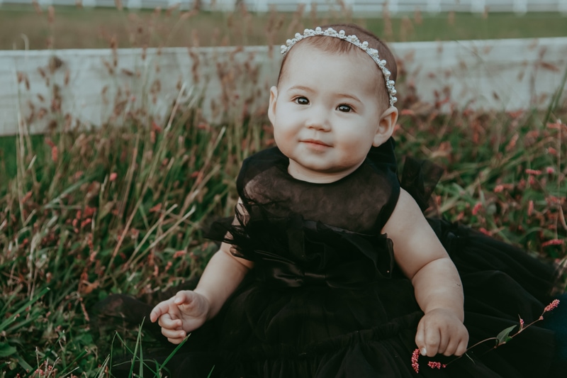 a baby girl in black dress is sitting and smiling during a fall outside family session by Bella Luna Photography in Fairfaix, VA