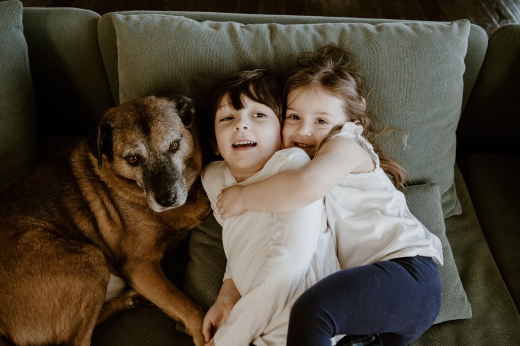 sister is hugging her brother on a couch with a dog during in home family session in loudoun county va
