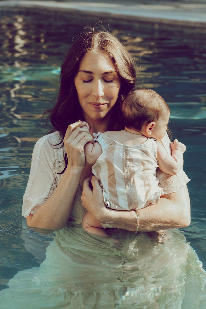 Mom is holding her baby's hand in the pool during a family photography session in Northern VA by Bella Luna Photography