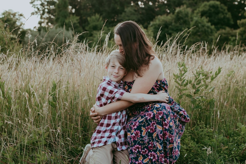 a mom is kissing her son while the son is looking at the camera during an outside family session by Bella Luna Photography