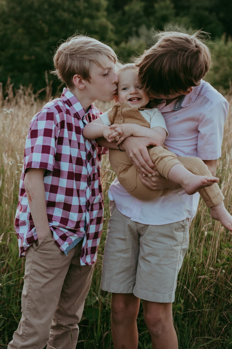 two older brothers kissing a younger brother during a family session in Loudoun County by Bella Luna Photography