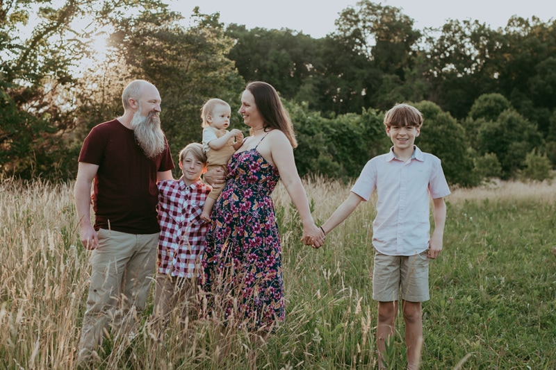 a mom is holding her young son and her older son while looking at dad during an outside family session in Loudoun County by Bella Luna Photography
