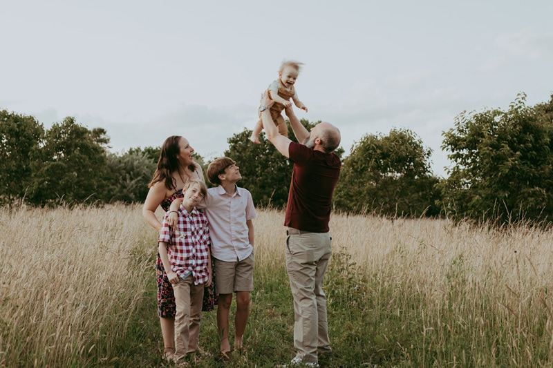a dad is throwing his son in the air while mom is looking at them during a family session in Leesburg, VA by Bella Luna Photography