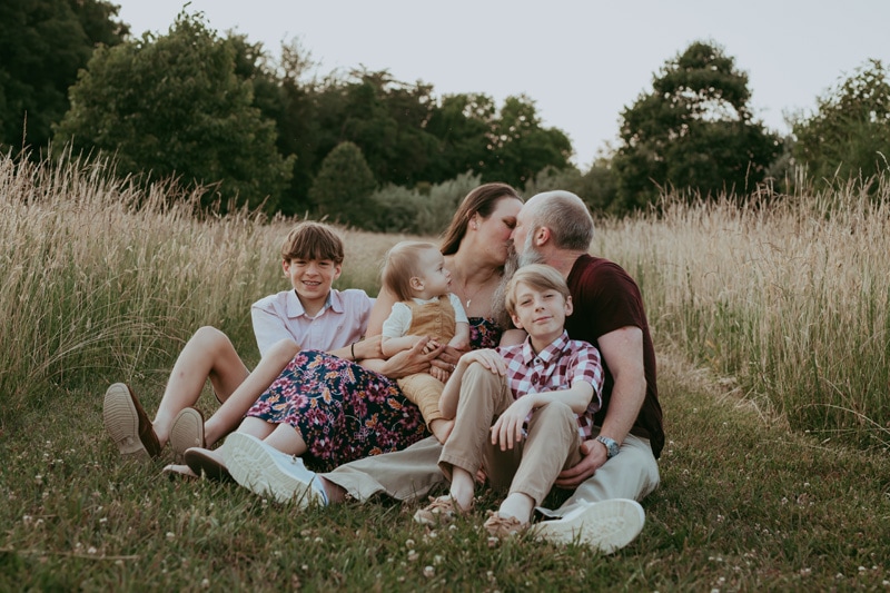 dad is kissing mom and posing with their kids during an outside family session in Leesburg, VA by Bella Luna Photography