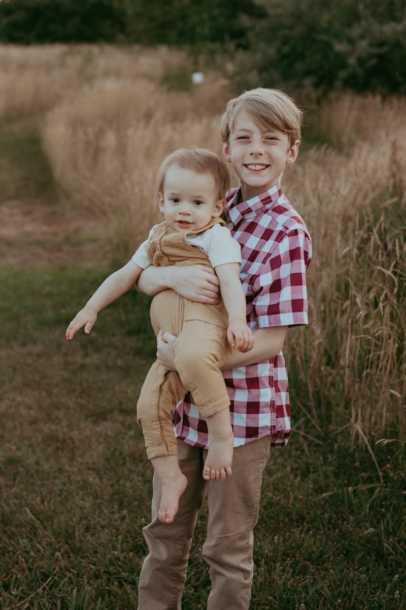 a big brother is holding a baby brother during an outside family session in Leesburg by Bella Luna Photography