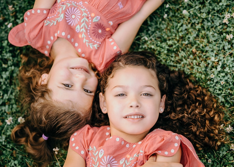 a close up of two sisters laying on green grass and looking up during a summer outside family session by Bella Luna Photography in Loudoun County